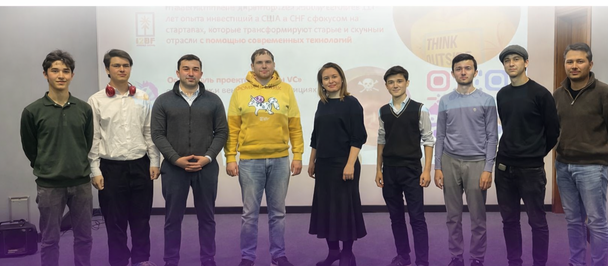 Group of people in casual clothes standing in a line on a stage in front of a logo banner.