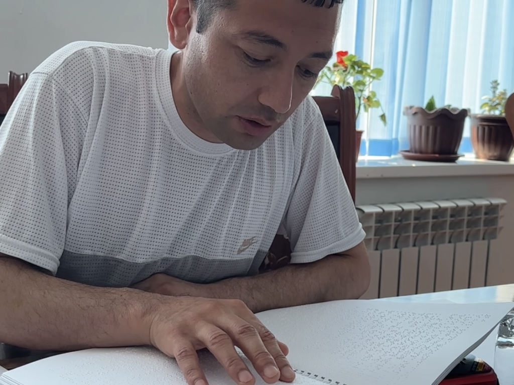 One of the members of the Karakul District Branch of the Blind Society of Uzbekistan is reading the guidebook in Braille