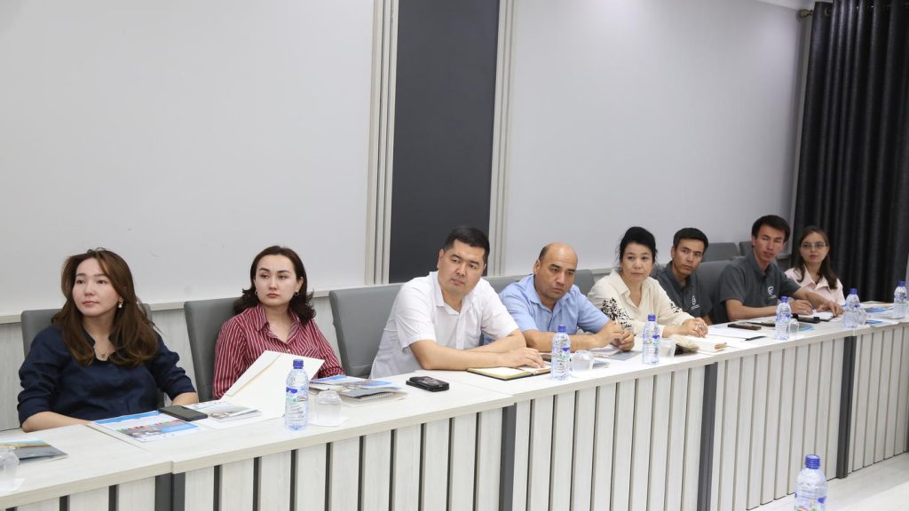 A group of eight people seated at a conference table, engaged in discussion.