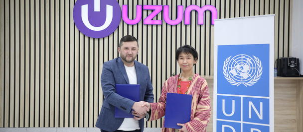 Two people shaking hands, holding blue folders, with a "Uzum" logo and UNDP banner in the background.