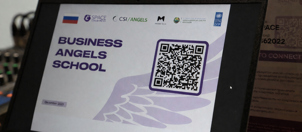 Tablet on a desk displaying a slide titled “Business Angels School” with a QR code.